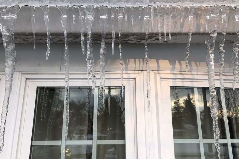 Long icicles hanging from a frozen rain gutter over two windows of a house